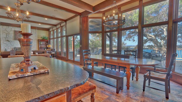A spacious dining area with a large wooden table and chairs, large windows offering a view of the outdoors, and a stone fireplace.