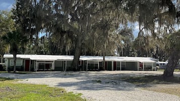 A row of motel buildings with a gravel parking area and trees with hanging moss.