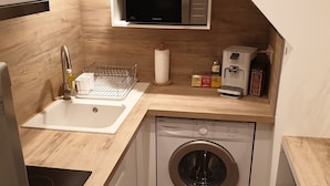 Een kleine keuken met een magnetron, koffiezetapparaat en wasmachine.
