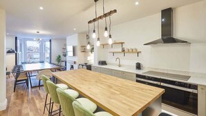 Une cuisine moderne dotée d’un îlot central, d’un four encastré et de luminaires suspendus.