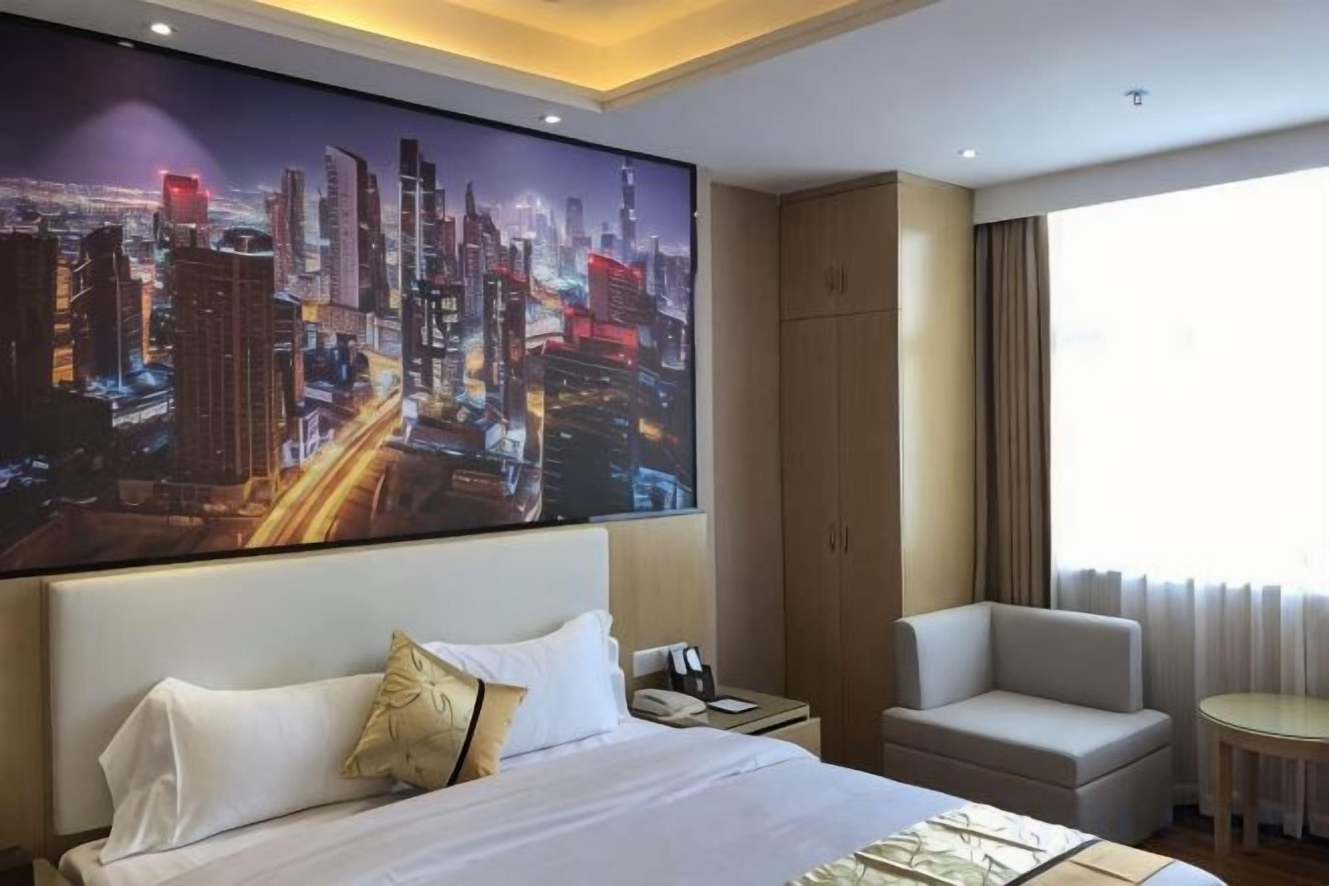 A hotel room with a large bed, a nightstand, a chair, a desk, and a cityscape painting on the wall.
