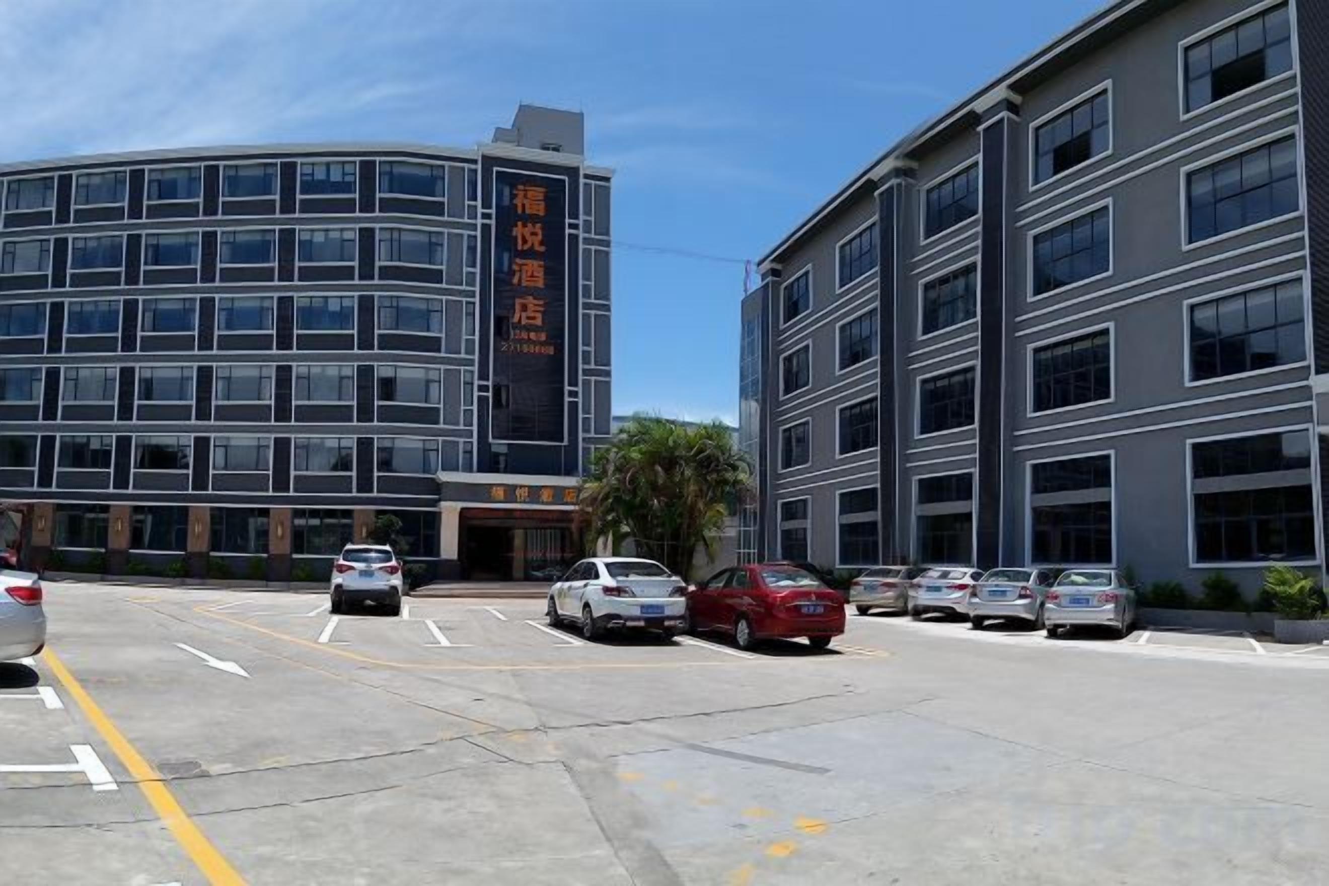 Um estacionamento com vários carros, um prédio de hotel com uma placa e um céu claro.