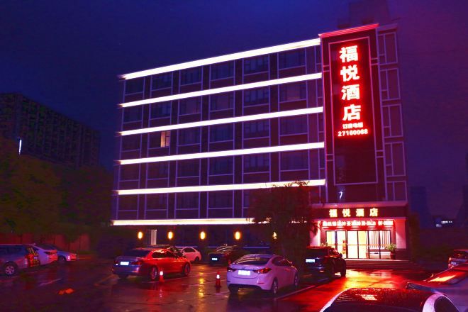 A multi-story hotel with a prominent red sign, a parking lot with several cars, and a building facade with horizontal lines.