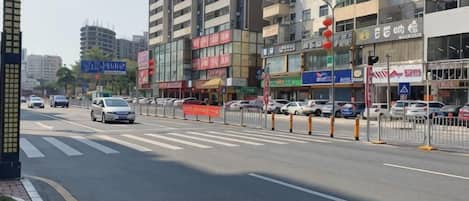 Un immeuble à plusieurs étages, doté d’enseignes commerciales, avec un passage piéton et des véhicules circulant dans une rue de la ville.