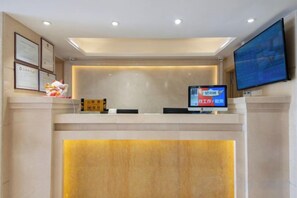 A hotel reception area with a reception desk, a flat-screen TV, and framed certificates on the wall. - Fuyue Hotel (Shenzhen)