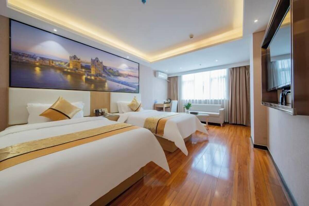 A hotel room with two beds, a large painting of a cityscape, a TV, and a window with curtains.