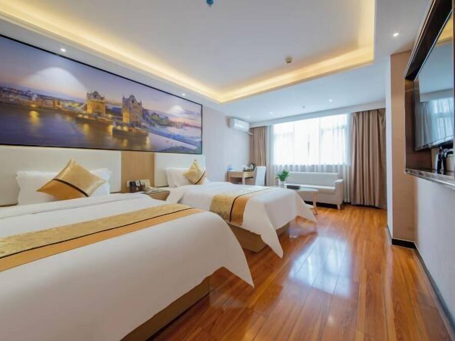 A hotel room with two beds, a large painting of a cityscape, a TV, and a window with curtains.