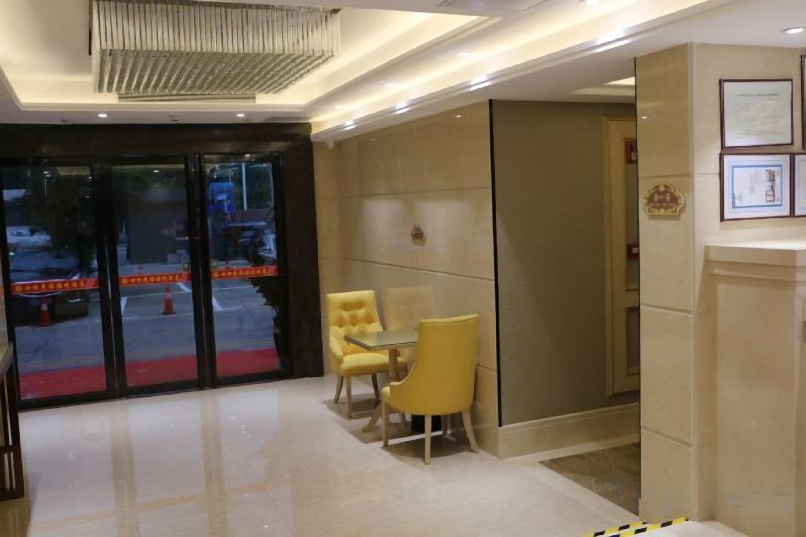 Un hall de hotel con una recepción, una zona de estar con sillas amarillas y un espejo grande.
