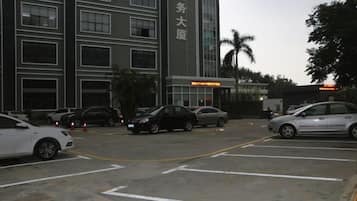 Un estacionamiento con varios autos, un edificio con letreros y una palmera.