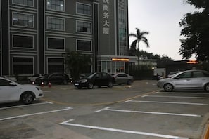 A parking lot with several cars, a building with signage, and a palm tree. - Fuyue Hotel (Shenzhen)