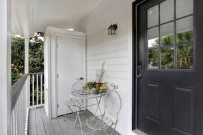 Eine Veranda mit einer weißen Tür, einem kleinen Tisch mit Stühlen und einem Blumentopf.