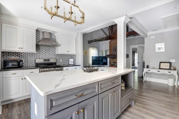 A modern kitchen with white cabinets, a marble island, and a chandelier.