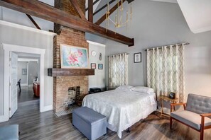 Un dormitorio con cama, un banco, una silla, una chimenea y vistas a otra habitación.