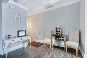 Una habitación con una consola blanca, dos sillas, una mesita con altavoces y un cuadro en la pared.