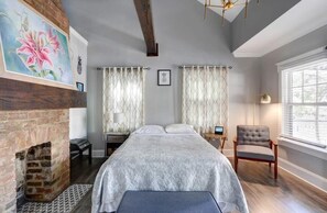 Een slaapkamer met een bed, een stoel, een open haard en een raam.