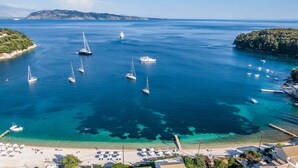A coastal area with clear turquoise waters, a sandy beach with sun loungers, and several sailboats anchored near the shore. - Kalami Beach - Villa Anastasia (Corfu)