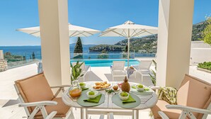 A table set for breakfast with a view of a pool and mountains. - Kalami Beach - Villa Anastasia (Corfu)