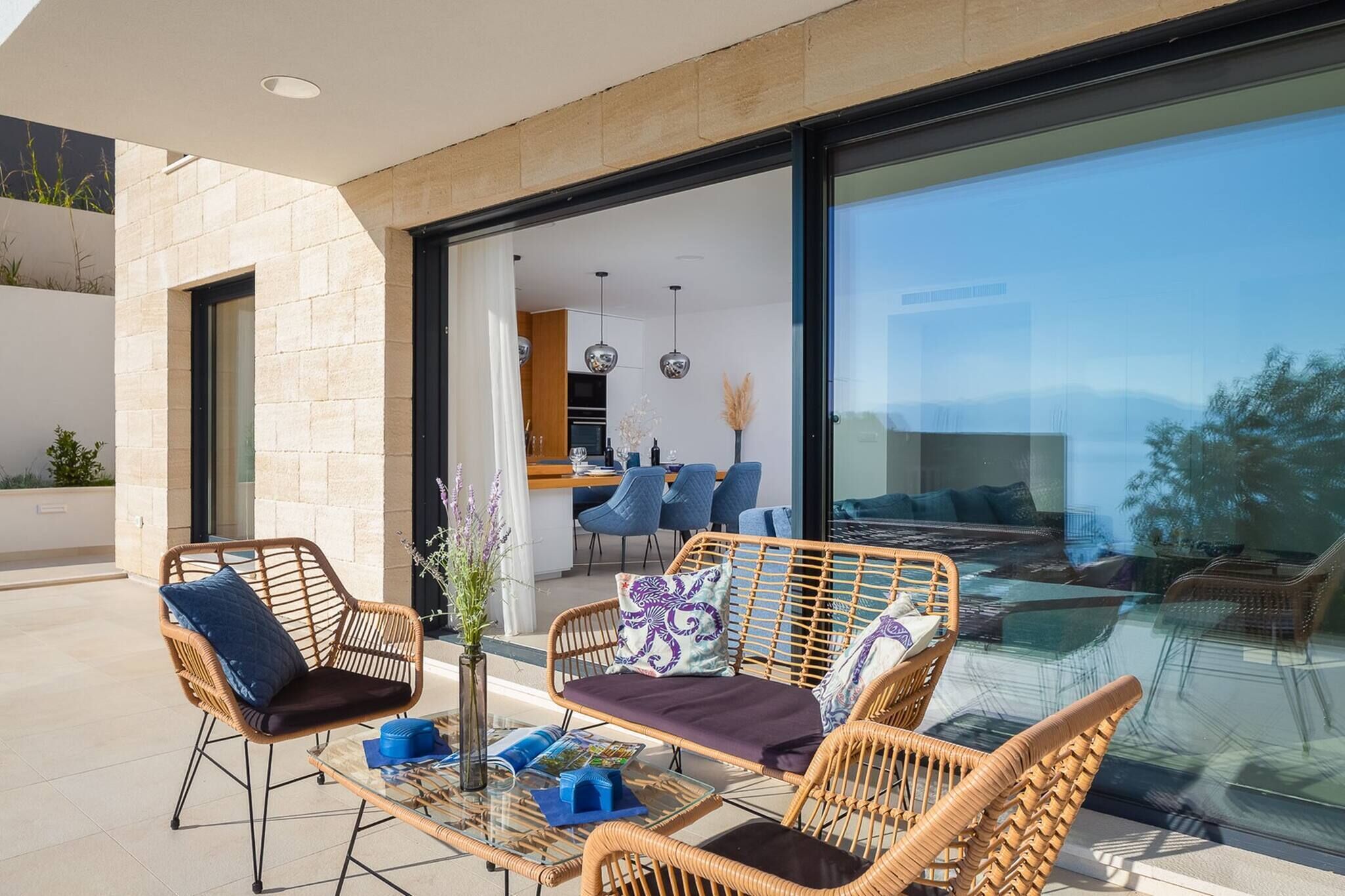Un espace extérieur aménagé avec des meubles en osier, une table en verre et une vue sur l’intérieur grâce à une porte vitrée.