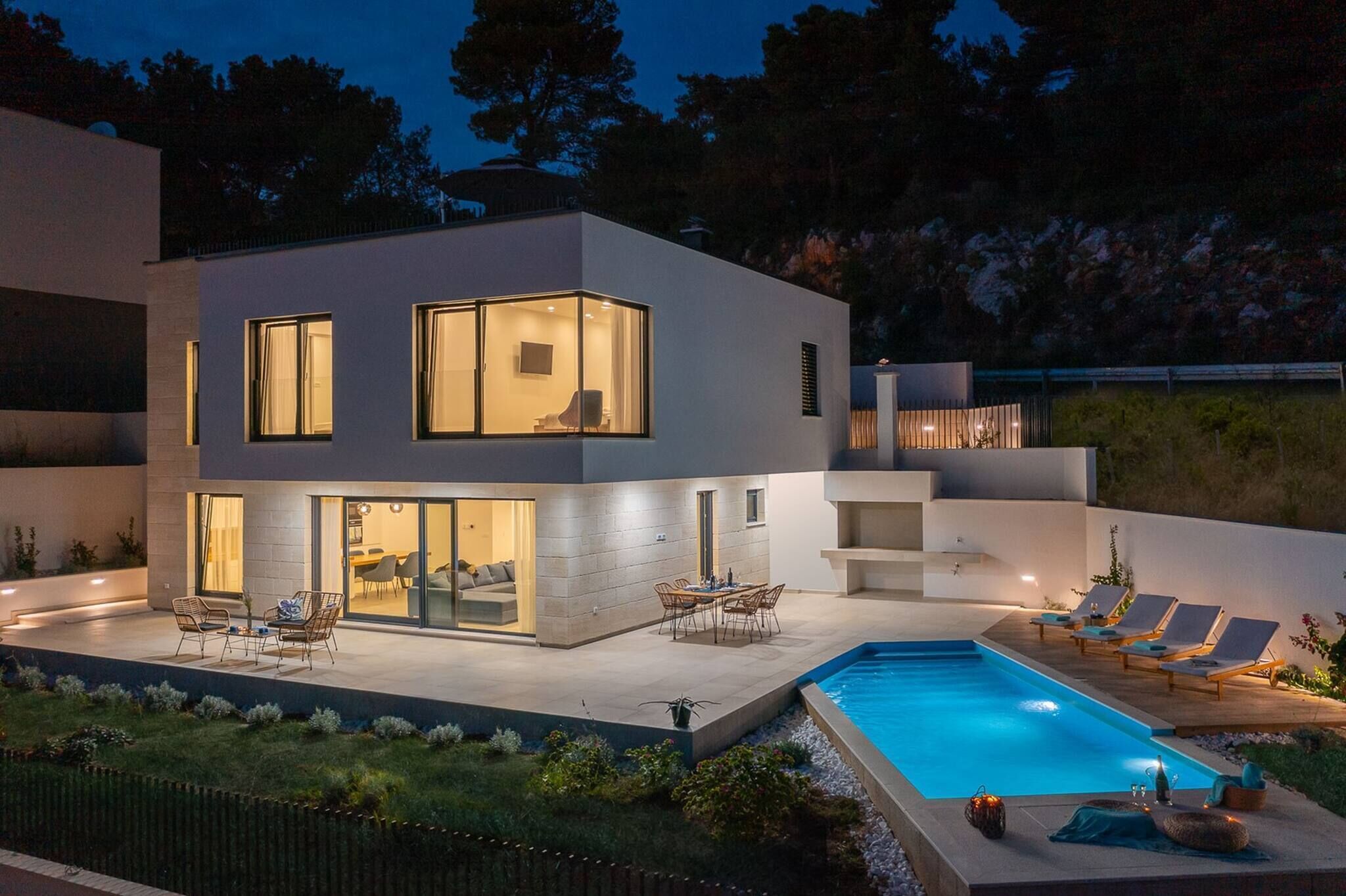 Une maison moderne à deux étages, dotée d’une piscine, d’un espace extérieur aménagé et d’un patio bien éclairé.
