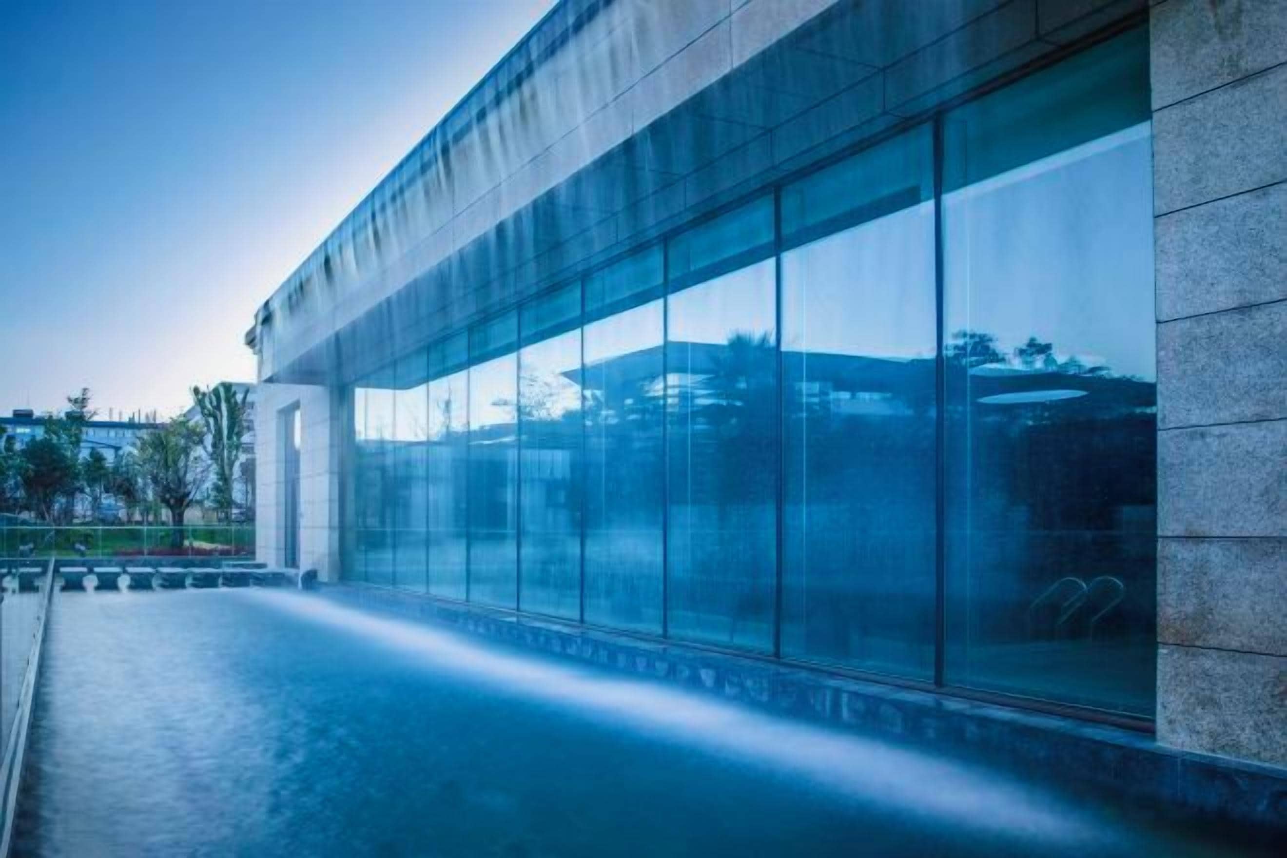 Ein modernes Gebäude mit großen Glasfenstern und einem spiegelnden Wasserspiel davor.