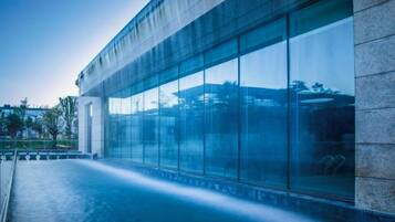 Ein modernes Gebäude mit großen Glasfenstern und einem spiegelnden Wasserspiel davor.