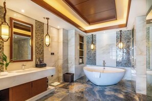 Un baño moderno con una bañera independiente, un mueble de tocador grande con espejo e iluminación decorativa.