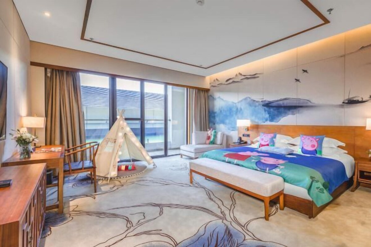Una habitación de hotel con cama, escritorio, silla, banco y un amplio ventanal.