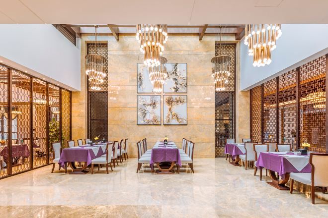 Un comedor amplio con mesas dispuestas para varios comensales, con techo alto y luminarias decorativas.