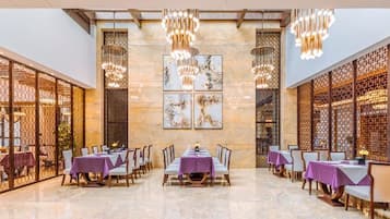 Un comedor amplio con mesas dispuestas para varios comensales, con techo alto y luminarias decorativas.