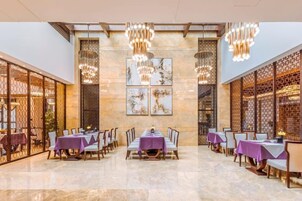 A spacious dining area with tables set for multiple guests, featuring a high ceiling and decorative lighting fixtures.