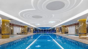 Una piscina interior moderna con una línea central, rodeada de zonas de estar y un techo decorativo.