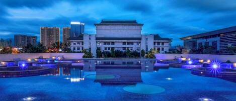 A building with a traditional architectural style, a reflective water feature in front, and modern high-rise buildings in the background.