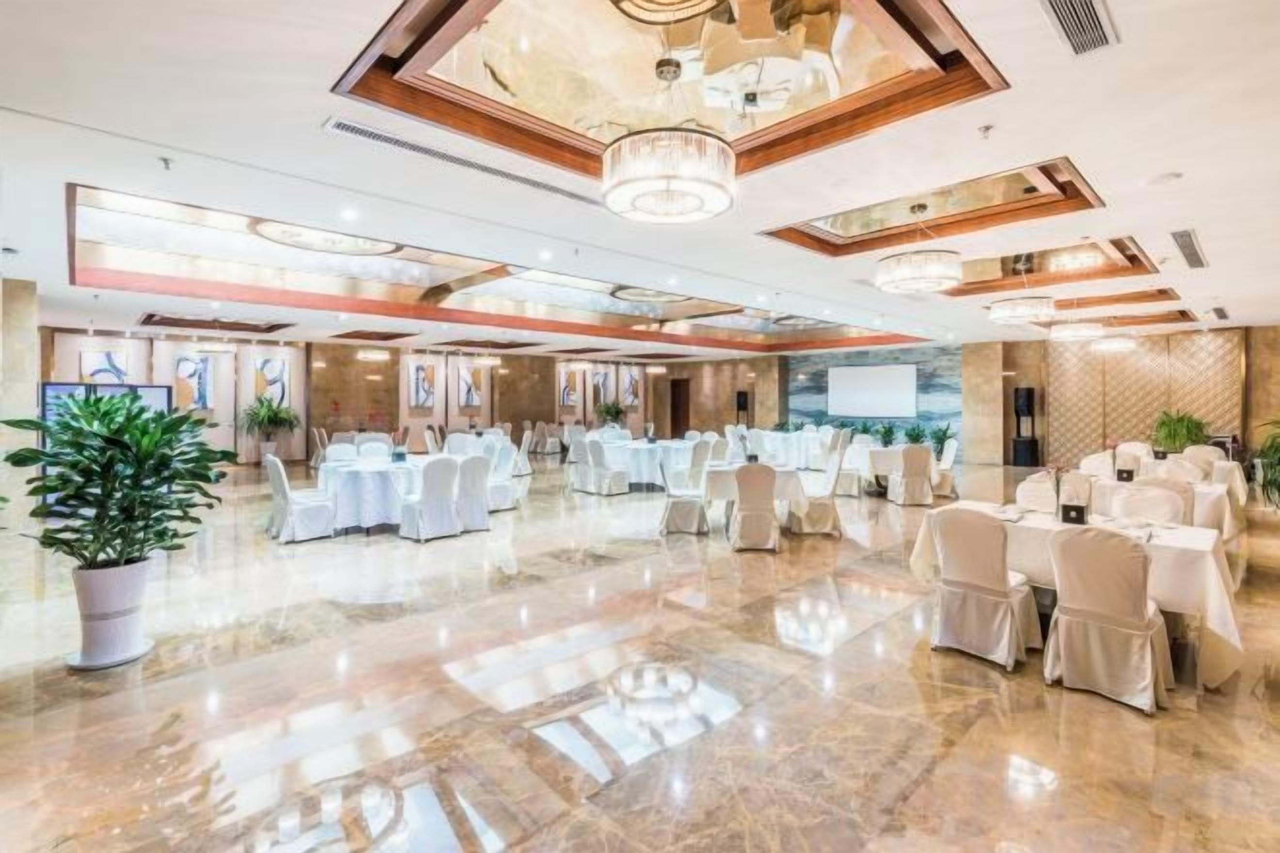 Un amplio salón de banquetes con varias mesas redondas, sillas y un piso de mármol pulido.