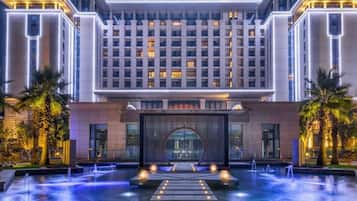Un hotel con fachada moderna, entrada central y una fuente en la parte delantera.