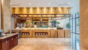 A modern hotel lobby with a marble reception desk, a central island with plants and decorative items, and large windows offering a view of the outdoors. - Yongchang Hotel (Baoshan)
