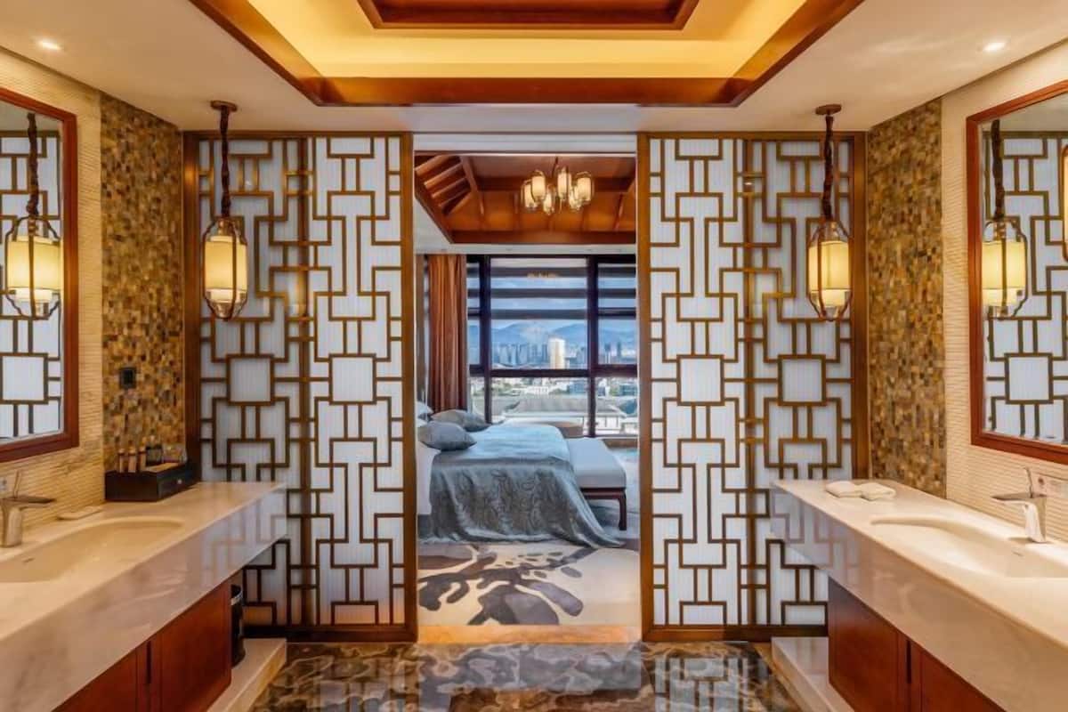 Une salle de bain moderne dotée d’un grand miroir, de deux vasques et offrant une vue sur la chambre à coucher à travers un paravent décoratif.