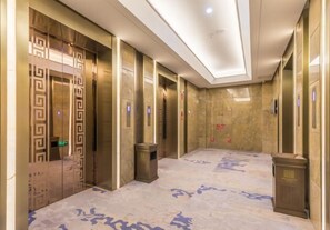 Un hall d’ascenseur moderne avec un sol à motifs, des portes d’ascenseur métalliques et une poubelle.