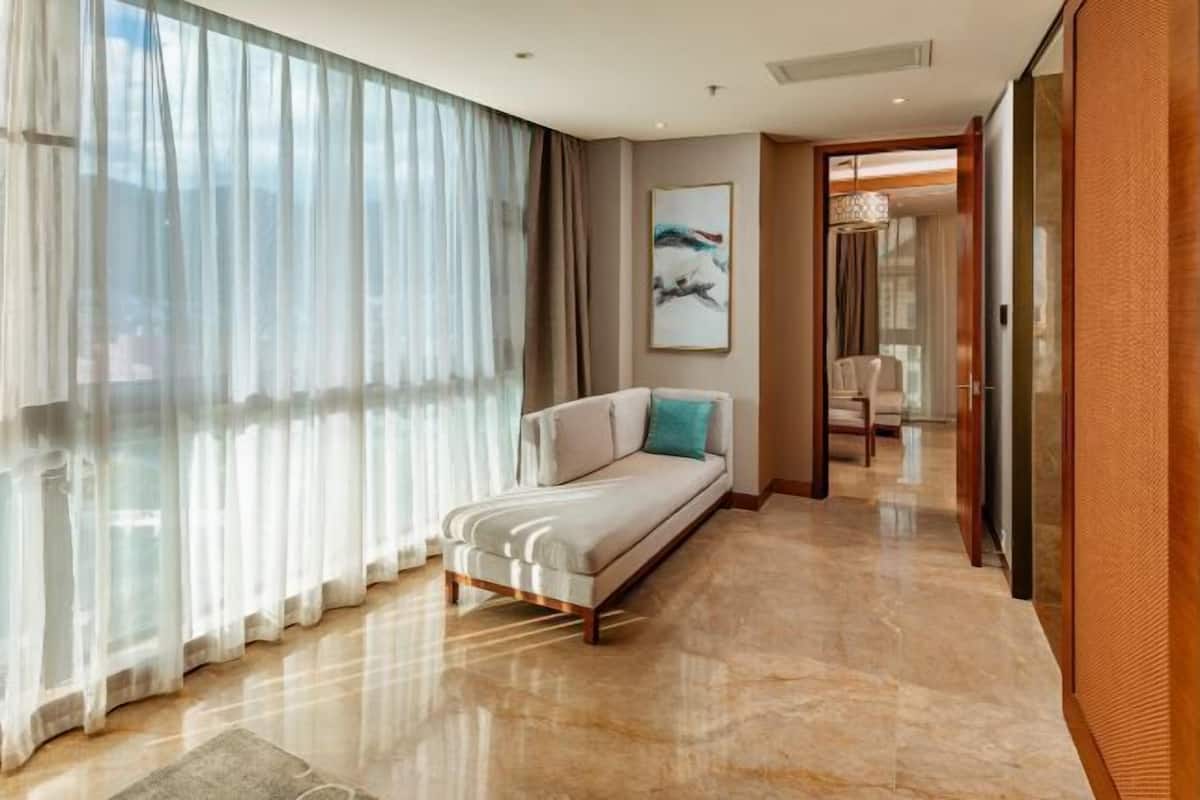 Une chambre d’hôtel moderne, dotée d’un canapé, d’une grande fenêtre avec des rideaux légers, d’un sol en marbre et d’une œuvre d’art encadrée au mur.