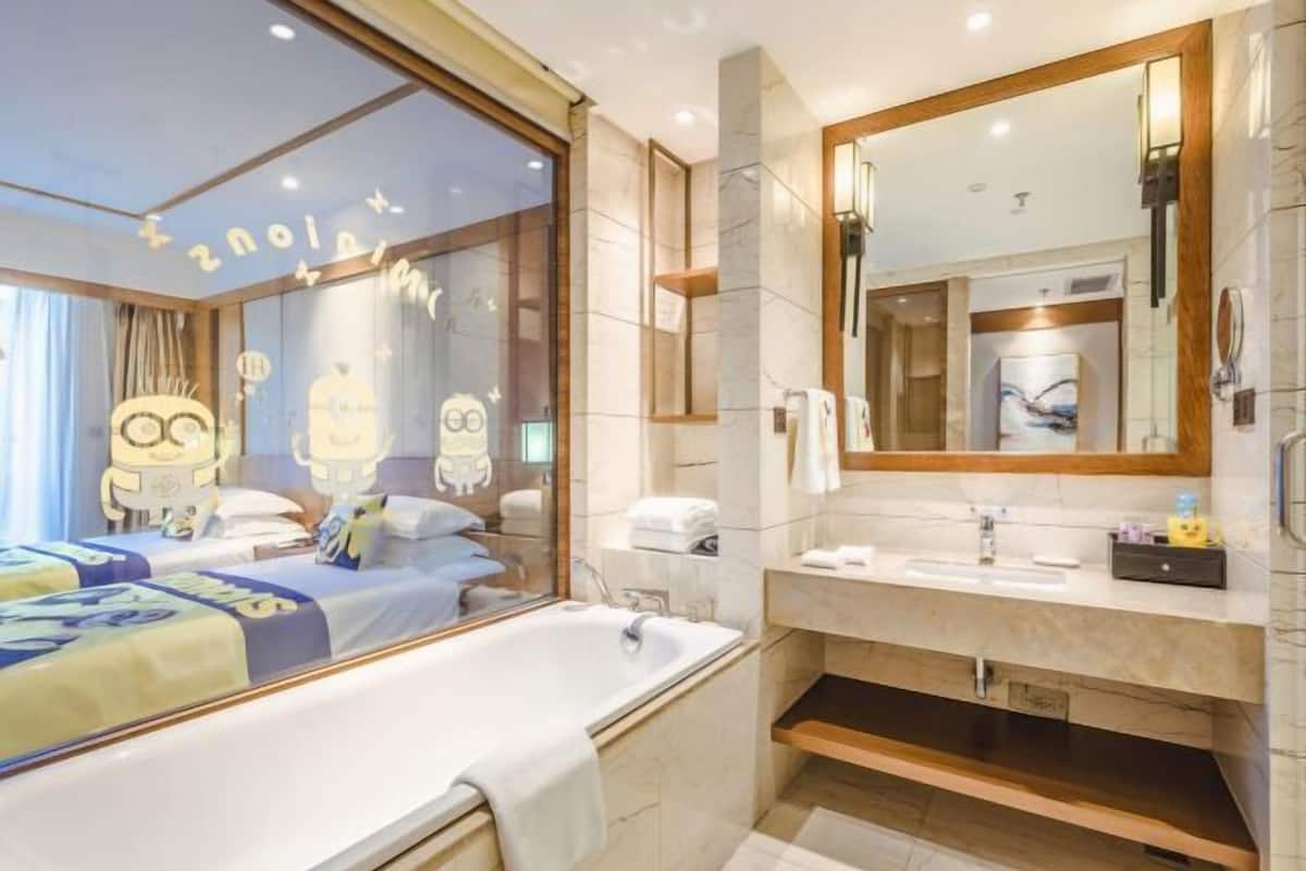 Une chambre d’hôtel moderne avec un grand lit, une salle de bain équipée d’un meuble-lavabo et d’un grand miroir.