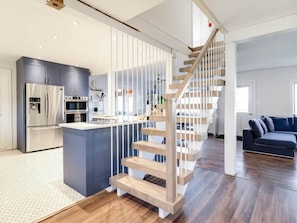 Eine moderne Küche mit einer zentralen Kochinsel, Edelstahlgeräten und einer Holztreppe mit weißen Geländern.