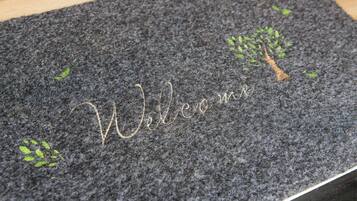 A dark textured mat with 'Welcome' embroidered in gold and small green leaf designs.