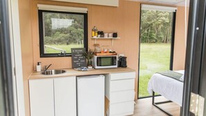 A compact kitchenette with a sink, microwave, and storage cabinets, a bed with a view of the outdoors, and a sign welcoming guests to the Tiny Home.