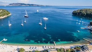 A coastal area with clear turquoise waters, a sandy beach with sun loungers, and several sailboats anchored near the shore. - Kalami Beach - Villa Mara (Corfu)