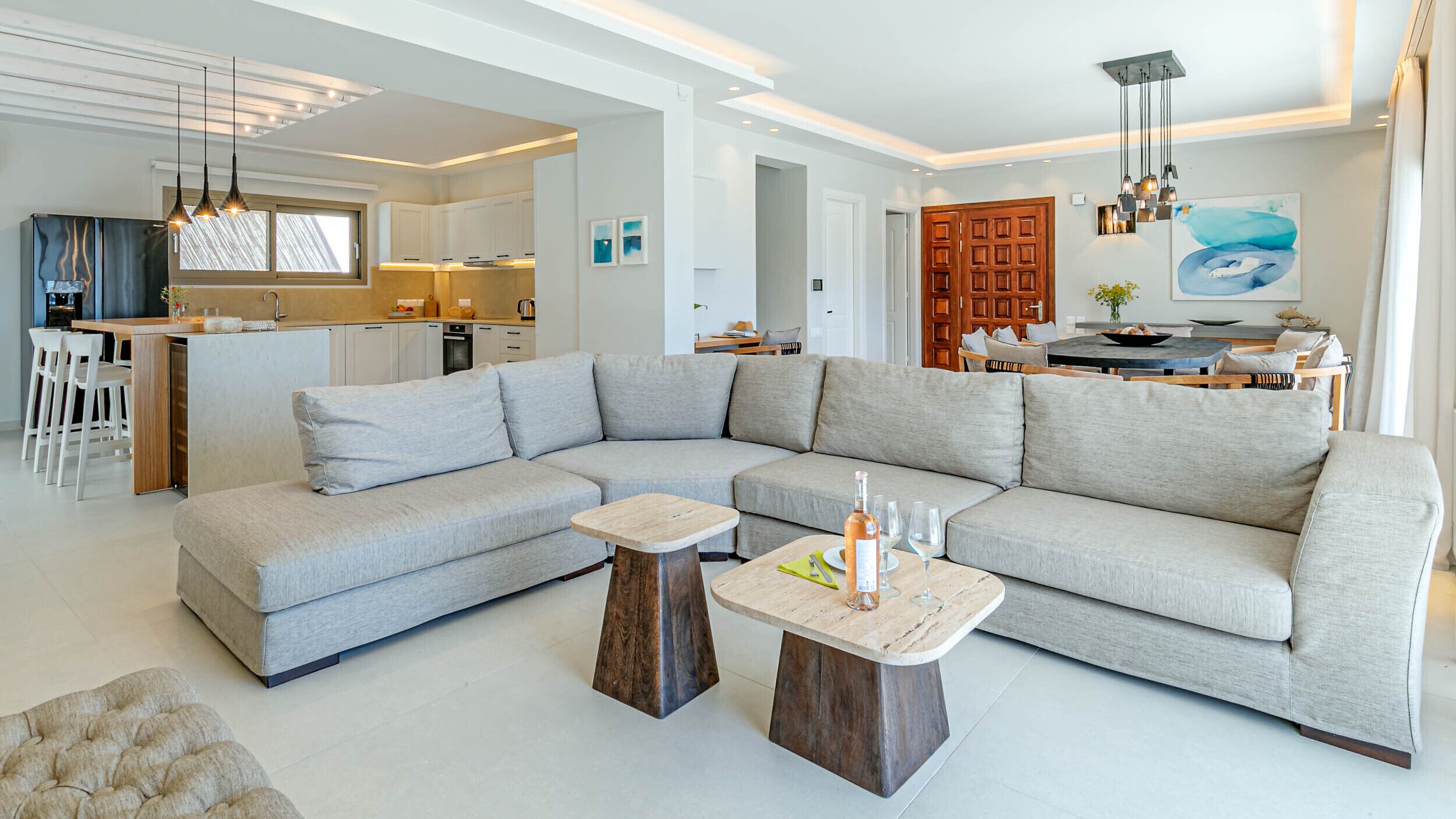 A modern living room with a large L-shaped sectional sofa, a wooden coffee table, and a dining area with a kitchen in the background.