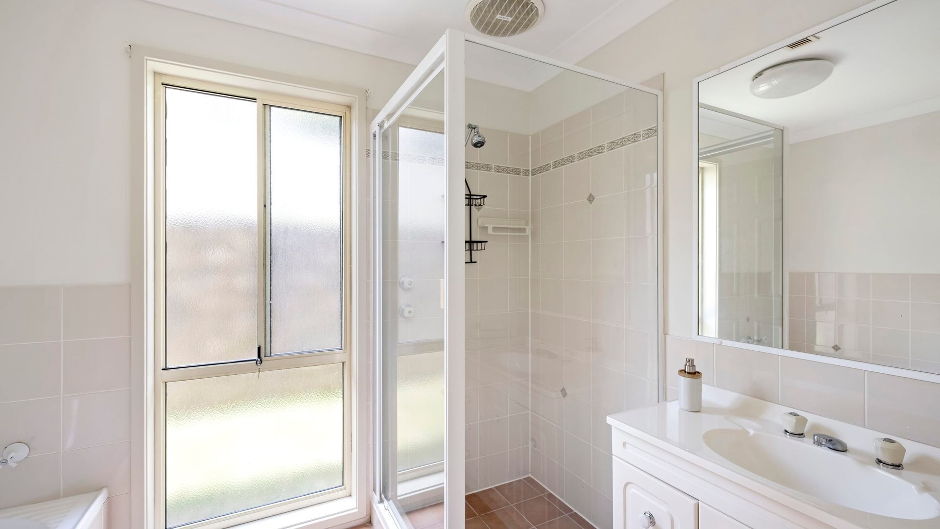 A bathroom with a large window, a shower, a sink with a mirror, and a toilet.