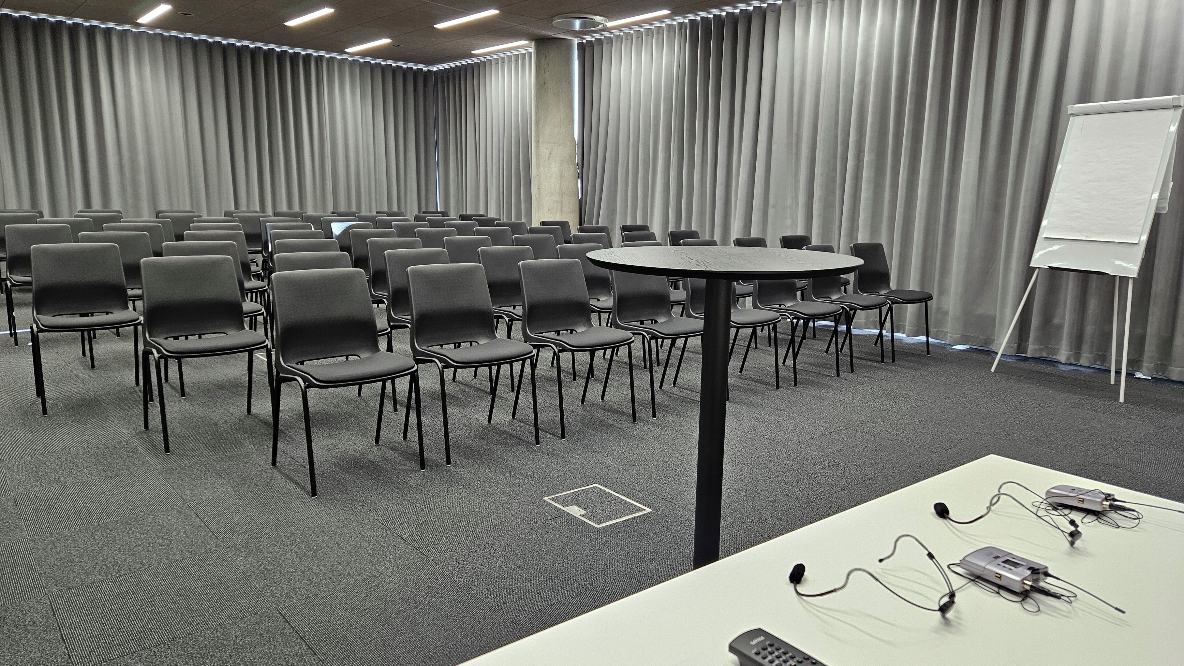 Un salón de conferencias con filas de sillas, una mesa redonda, una pizarra y un proyector.