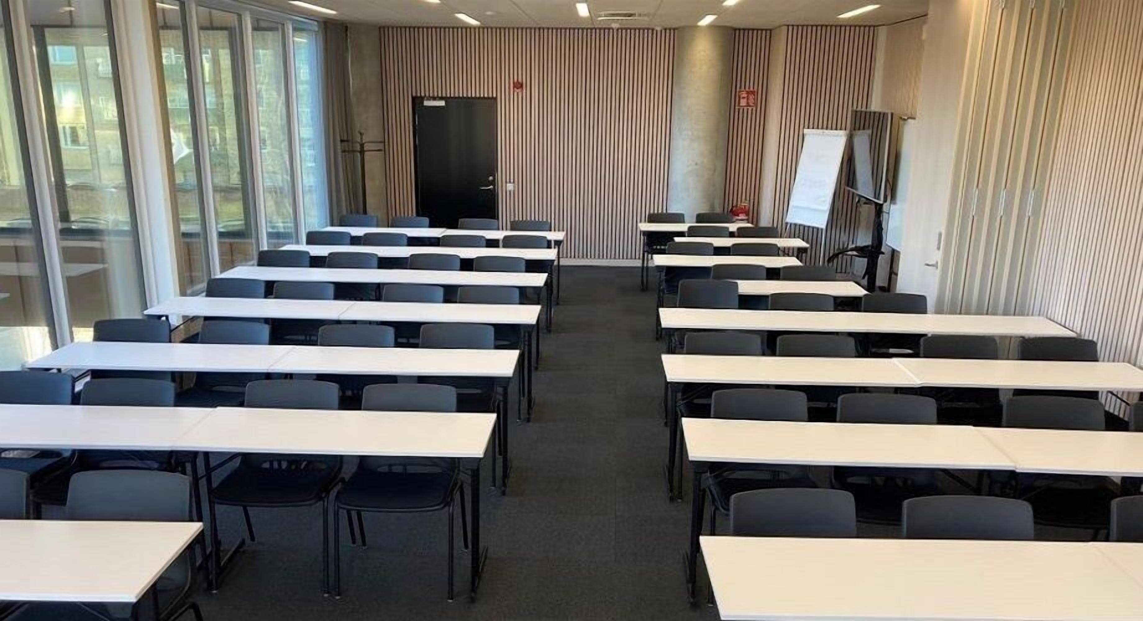 A conference room with multiple tables and chairs, a whiteboard, and a projection screen.