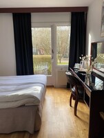 Habitación de hotel con cama, escritorio, silla, radiador y ventana con cortinas.