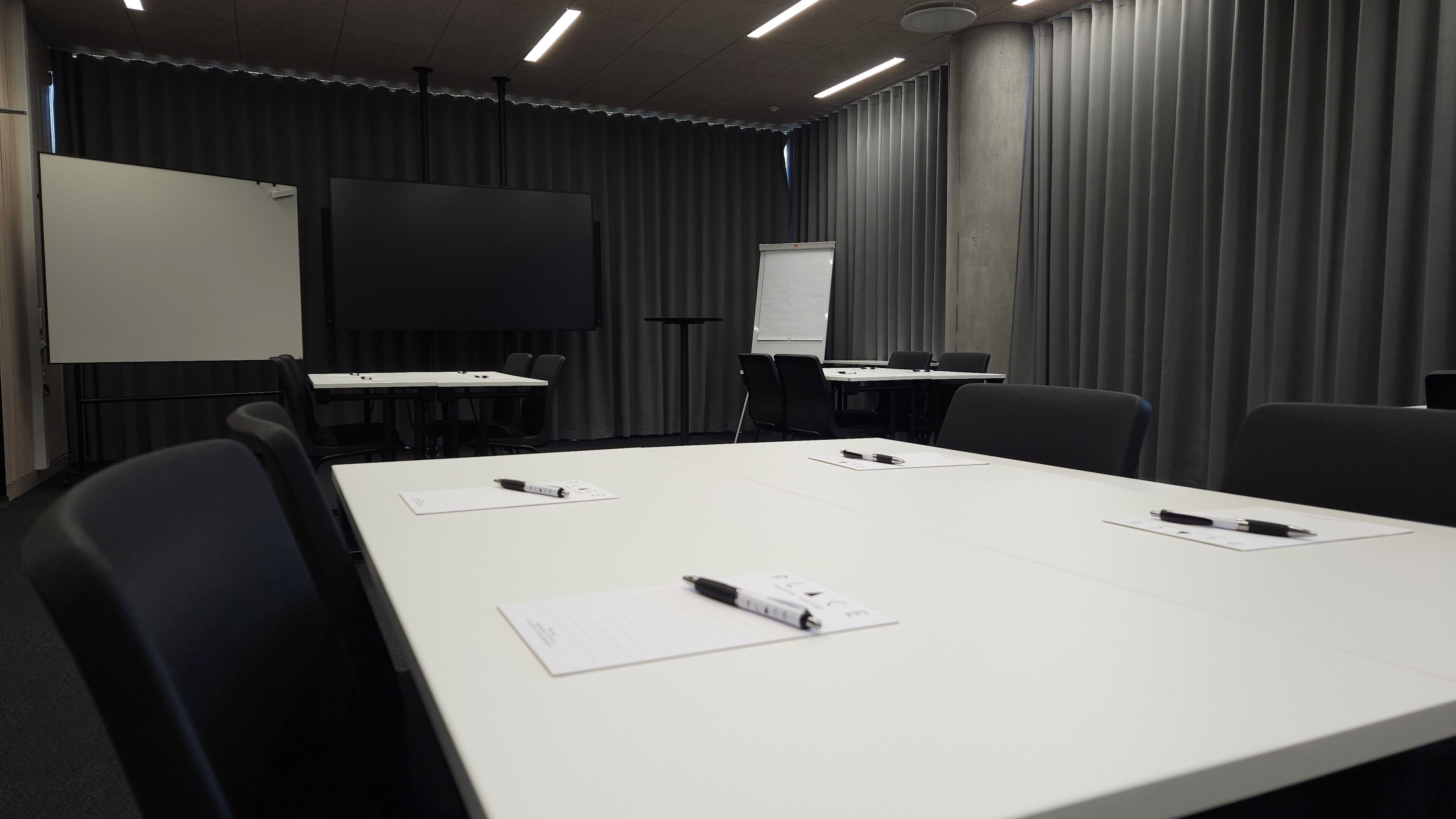 Une salle de conférence équipée d’une longue table, de chaises, d’un tableau blanc et d’un écran de projection.
