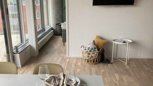 Un comedor moderno con una mesa blanca dispuesta para dos personas, un televisor montado en la pared y vistas al balcón exterior.